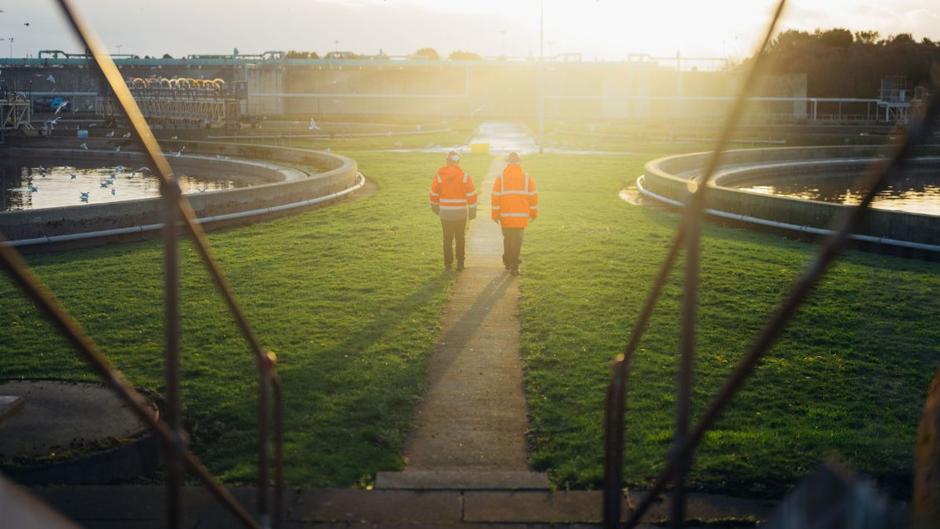 Two Veolia Ecofactory employees walk through wastewater treatment facility at sunset