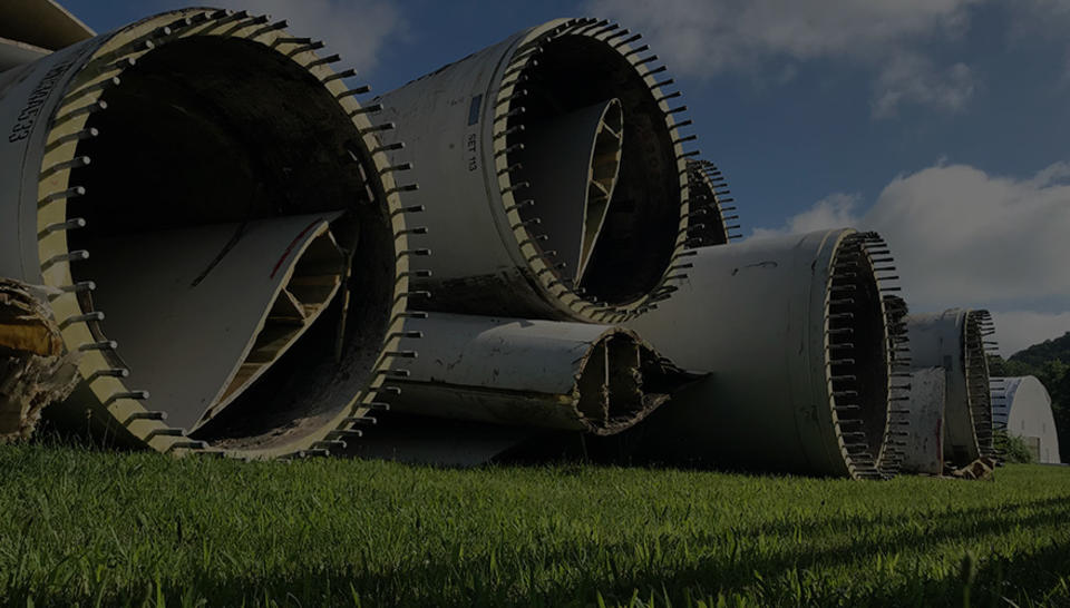 A pile of retired wind turbine blades sit on the grass