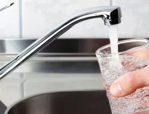 A hand fills a drinking glass with water from a kitchen faucet