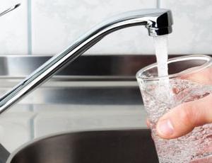 A hand fills a drinking glass with water from a kitchen faucet