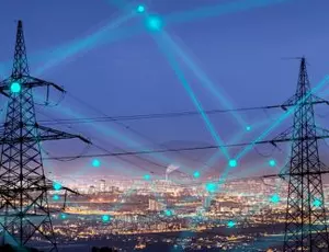 A set of electric transmission lines is seen in the foreground with a city in the background