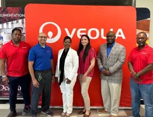 The team takes a photo in front of a Veolia logo