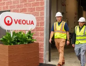 Two Veolia employees walk by a facility with a Veolia sign in the front