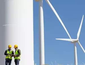Two people wearing safety vests stand at the base of a wind turbine tower