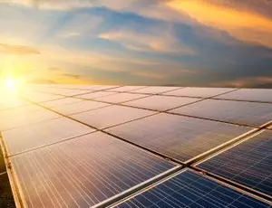 A solar panel array is seen with the sun rising in the background