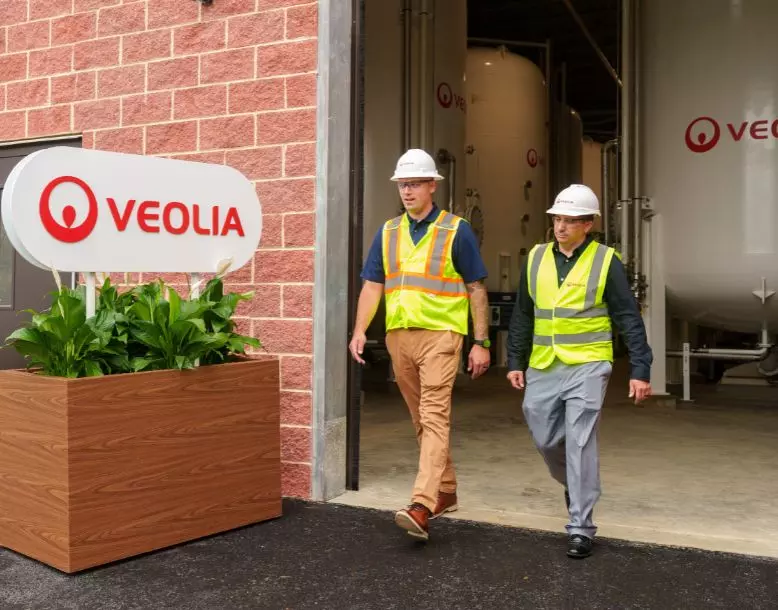 Two Veolia employees walk by a facility with a Veolia sign in the front