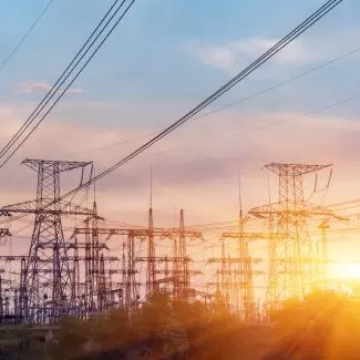 Electric transmission lines seen with a sun on the horizon in the background