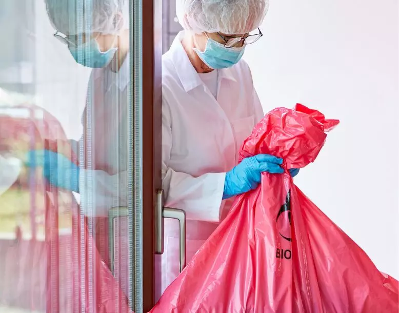 A person in a clinic carries a plastic bag labeled hazardous