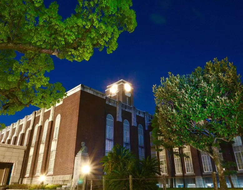 A campus building is seen at night with outdoor lights turned on