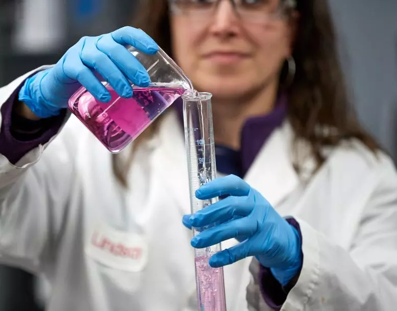 A lab technician pours from a beaker into a test tube