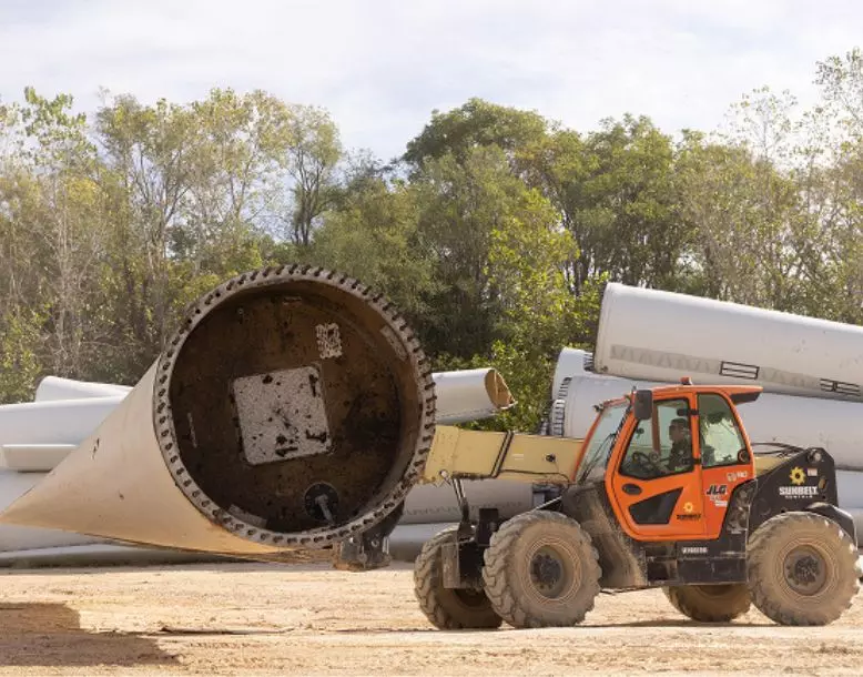 A wind turbine blade is transported on a forklift within a facility