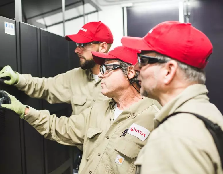 Three Veolia employees look together at a piece of equipment