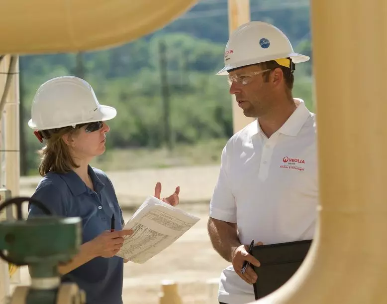 Two Veolia employees stand outside in a water treatment facility, having a discussion